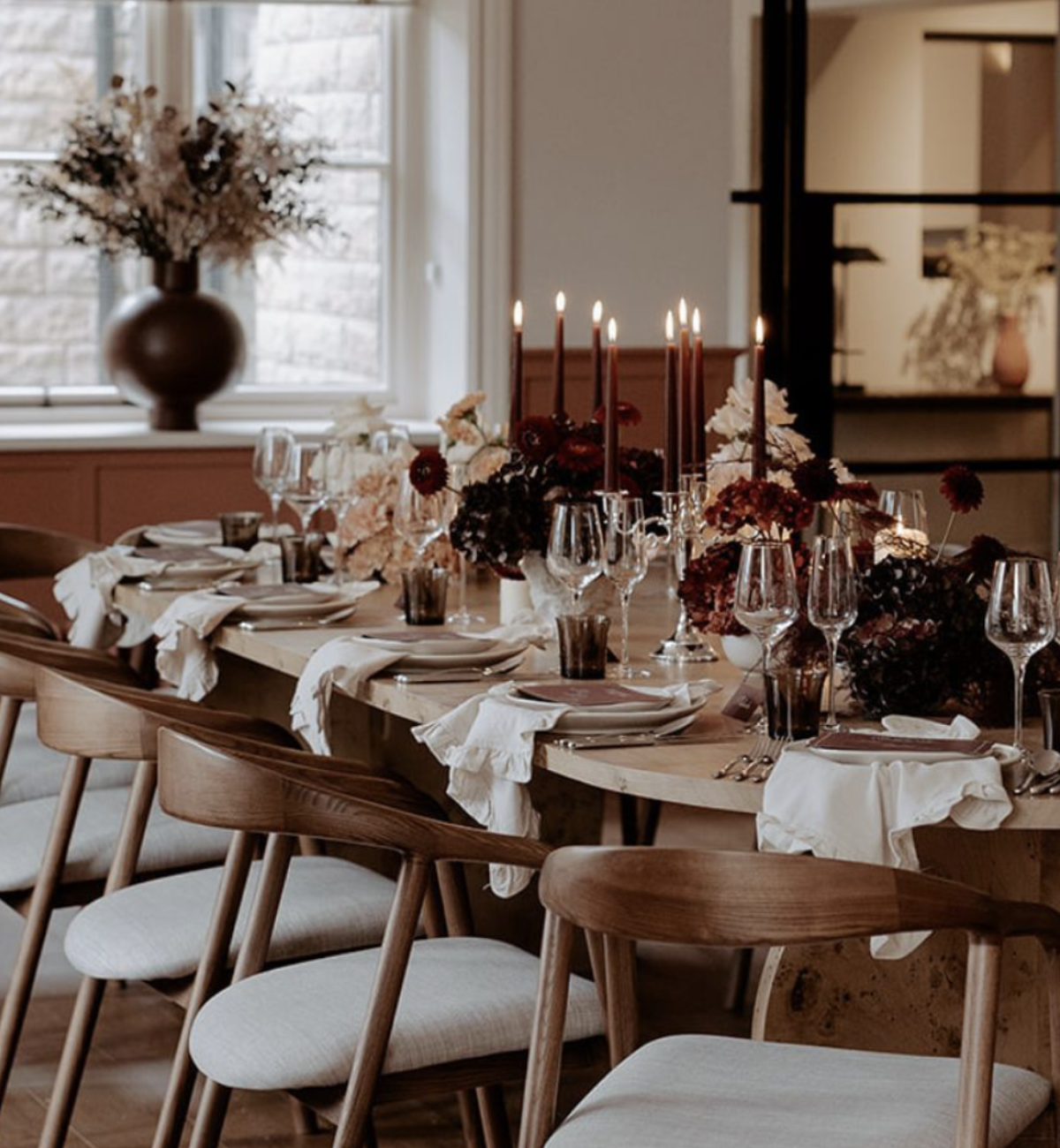 A long wooden table laid for dinner with candles, glassware and dried flowers
