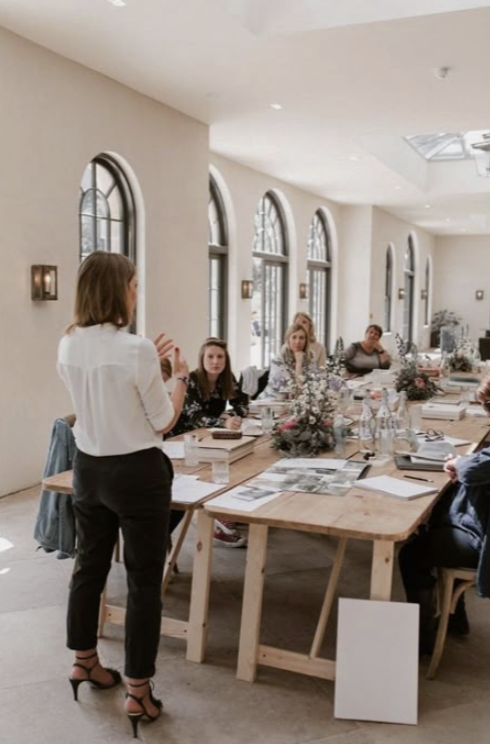 A Luminous corporate workshop in a bright, airy room with a presenter and a group seated around long tables