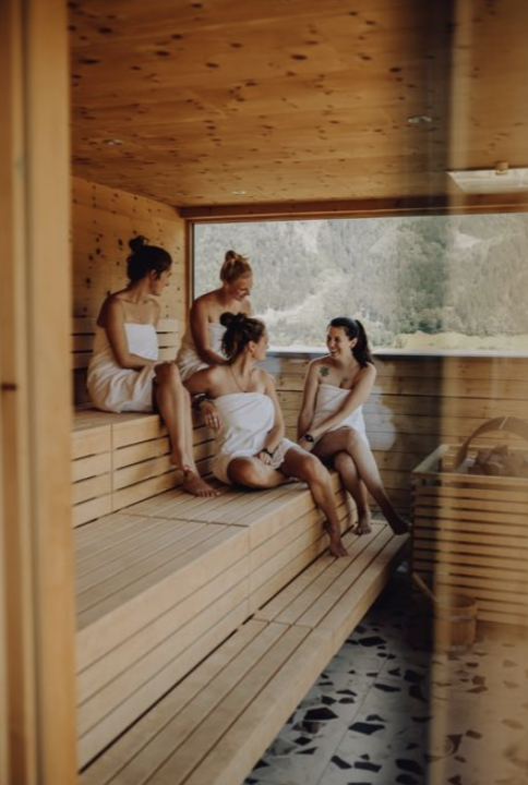 Women relaxing together in a wooden sauna looking out onto forest