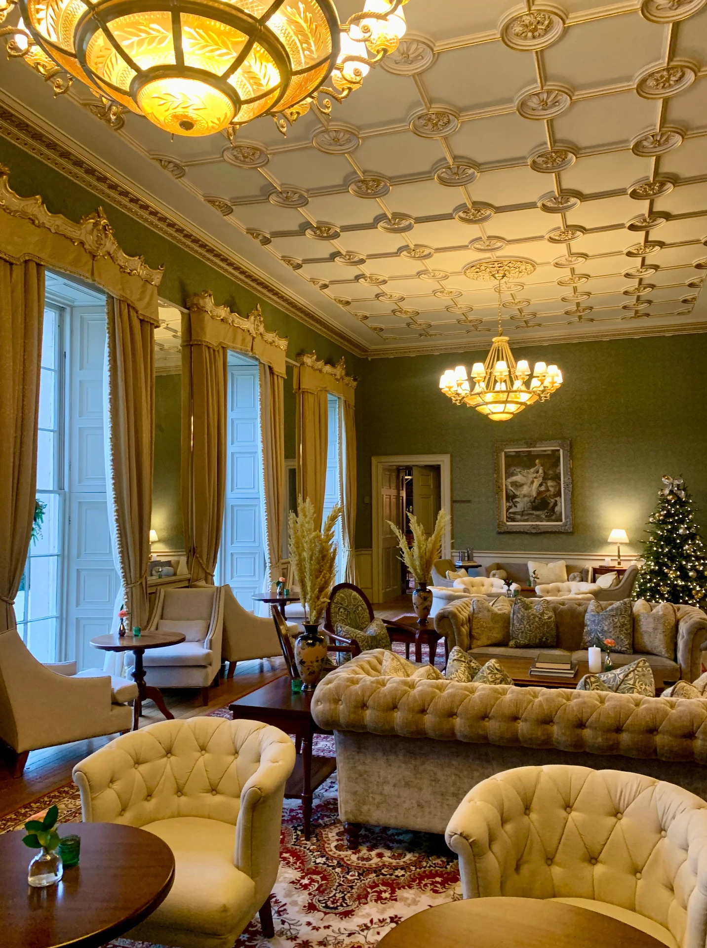 A grand lounge at Carton House with tall curtained windows, tufted sofas and a decorated Christmas tree
